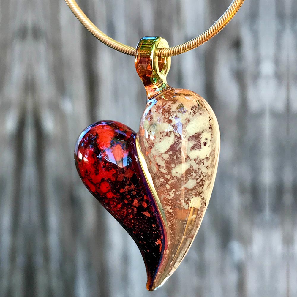 A garnet-red and yellowish-tan glass heart memorial pendant hangs from a yellow gold snake chain.